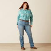 Woman wearing a light blue patterned shirt and jeans on a plain background